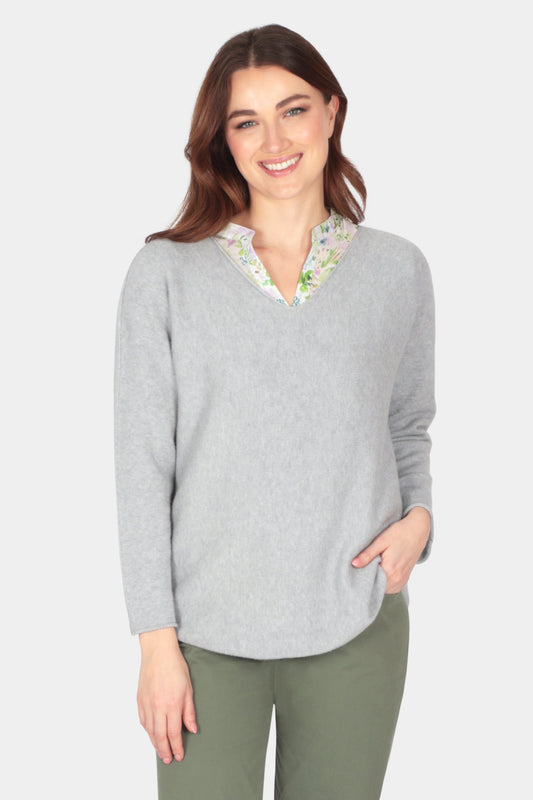 A soft yarn silver grey v neck spring summer cloud knitwear jumper 
 over a floral light blouse and khaki trousers 